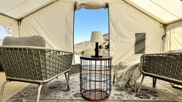A tent interior with two wicker chairs, a round table with a lamp, and a patterned rug.