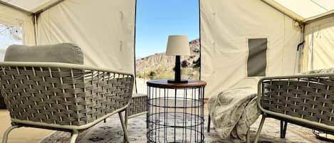 A tent interior with two wicker chairs, a round table with a lamp, and a patterned rug.