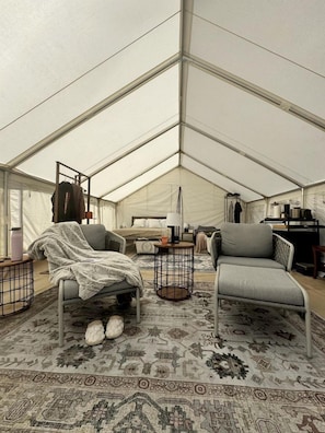 A tented room with a bed, two chairs, a small table, and a wardrobe.