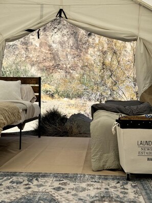 A tented room with a bed, a small table, and a bag labeled 'LAUNDRY NEW ESTABLISHMENT.'