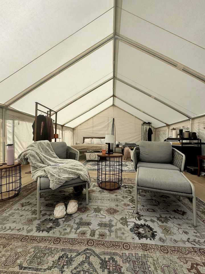 A tented room with a bed, two chairs, a small table, and a wardrobe.