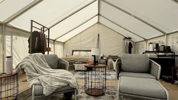A tented room with a bed, two chairs, a small table, and a wardrobe.