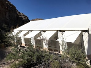 A row of white tents with a rocky cliff in the background.