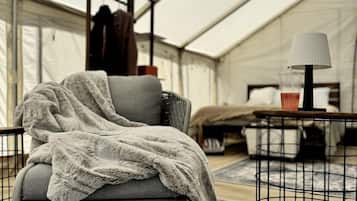 A tented room with a grey chair, a small table with a lamp, and a pair of slippers on the floor.