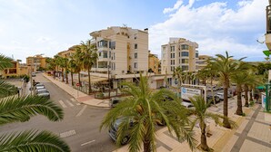 Un immeuble à plusieurs étages, doté d’un toit plat, d’une enseigne indiquant « Fabrication de cuisines de qualité » et bordé de palmiers le long du trottoir.