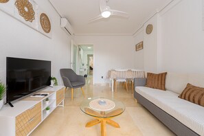 Una sala de estar con televisor, sofá, sillas y una mesa de centro de vidrio.
