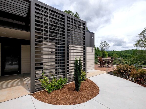 A modern building with a metal facade, a patio area with outdoor furniture, and a view of a green landscape.