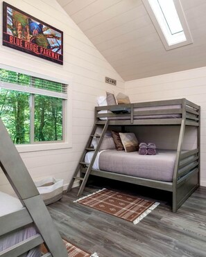 A bunk bed room with a window, a ladder, a 'GO Hike' sign, and a 'Blue Ridge Parkway' poster.