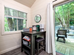 A room with a table, a chair, a coffee maker, and a window with blinds.