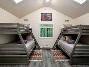 A dormitory room with bunk beds, a skylight, a window with a view of trees, and a 'GO Hike' sign.