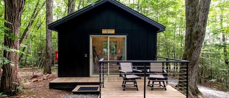 Una cabaña con terraza de madera, dos sillas y una puerta de cristal.