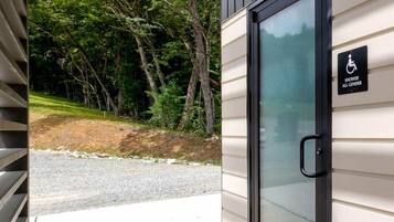 Entrada de un edificio con puerta de cristal, señal de accesibilidad para personas con movilidad reducida y un camino de hormigón que conduce a una zona de grava.