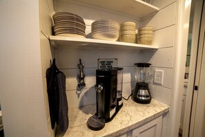 Une cuisine équipée d’une machine à café, d’un mixeur et d’étagères où sont empilées des assiettes.