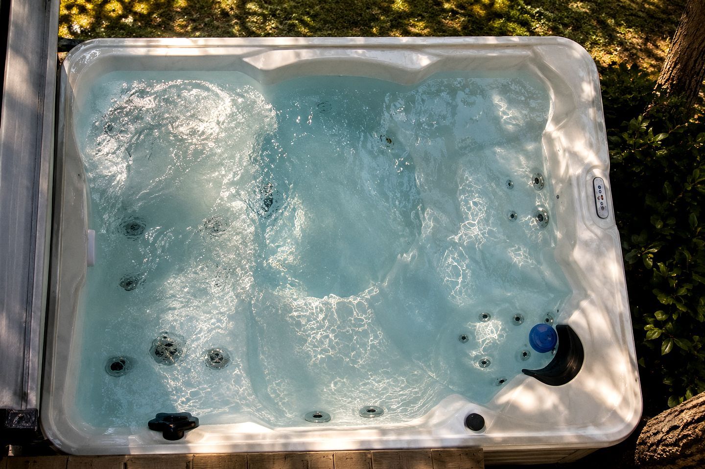 A hot tub with multiple jets, surrounded by a wooden deck and greenery.