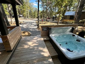 Eine Holzterrasse mit Whirlpool, umgeben von Bäumen und einem Kiesweg.