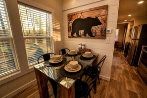 A dining area with a glass table, chairs, and plates. There is a bear silhouette artwork on the wall. - The Getaway at The Retreat in Monteagle, TN (Monteagle)