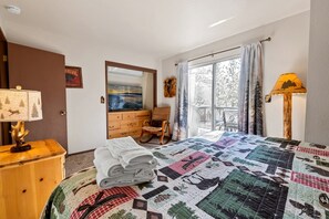 Ein Schlafzimmer mit einem großen Bett, einem Schminktisch, einem Stuhl, einem Gemälde und einem Fenster mit Vorhängen.