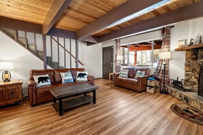 Un salon spacieux doté d’un plancher en bois, d’un canapé en cuir marron, d’une table basse en bois et d’une cheminée en pierre.