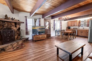 Un vaste espace de vie comprenant un coin salon avec cheminée, une table à manger et une cuisine dotée de meubles en bois.