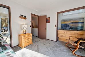 Quarto com cômoda de madeira, televisão e porta que dá para outro aposento.