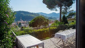 A balcony with a table and chairs, overlooking a town with a church tower and hills. - Room 'Stanza in Villa Magica' with Wi-Fi and Air Conditioning (Credaro)