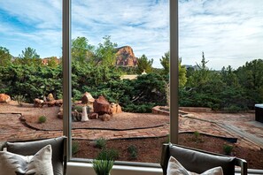 Vue depuis l’intérieur d’une pièce dotée de grandes fenêtres donnant sur un espace extérieur aménagé, avec des rochers et des arbres.