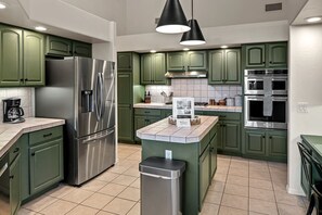 Une cuisine avec des meubles de couleur verte, des appareils électroménagers en acier inoxydable, une machine à café et un panneau d’accueil.