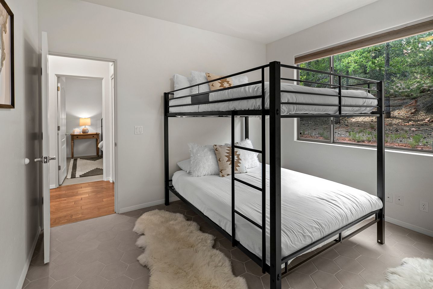 A bunk bed with a window view, a door leading to another room, and a rug on the floor.