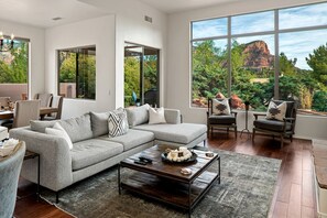 Un salon moderne comprenant un canapé d’angle, deux fauteuils, une table basse et de grandes fenêtres donnant sur un paysage montagneux.