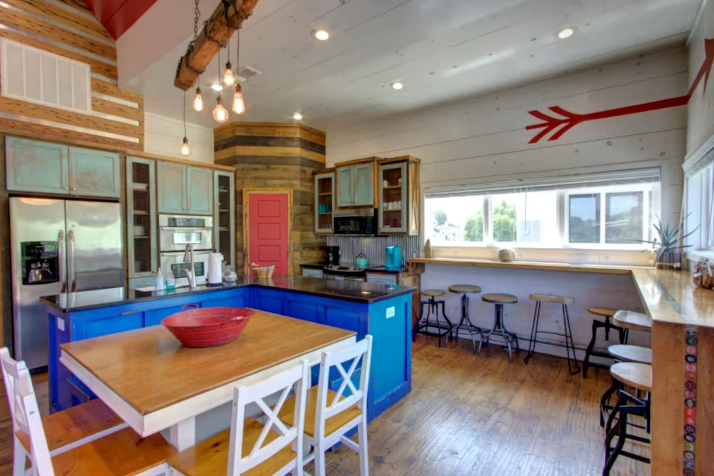 Una cocina con armarios azules, una isla de madera y una puerta roja.