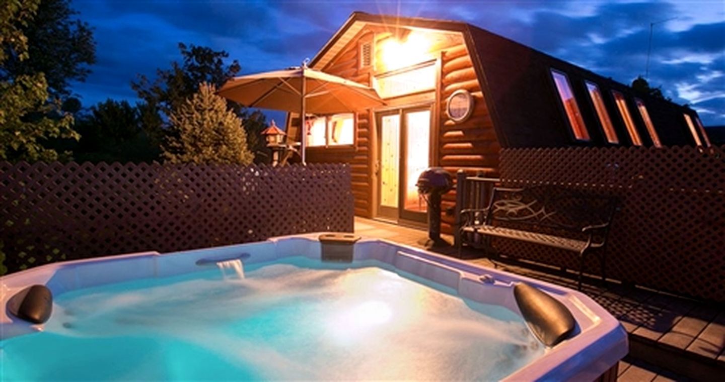 A wooden cabin with a hot tub, a patio, and a covered seating area.