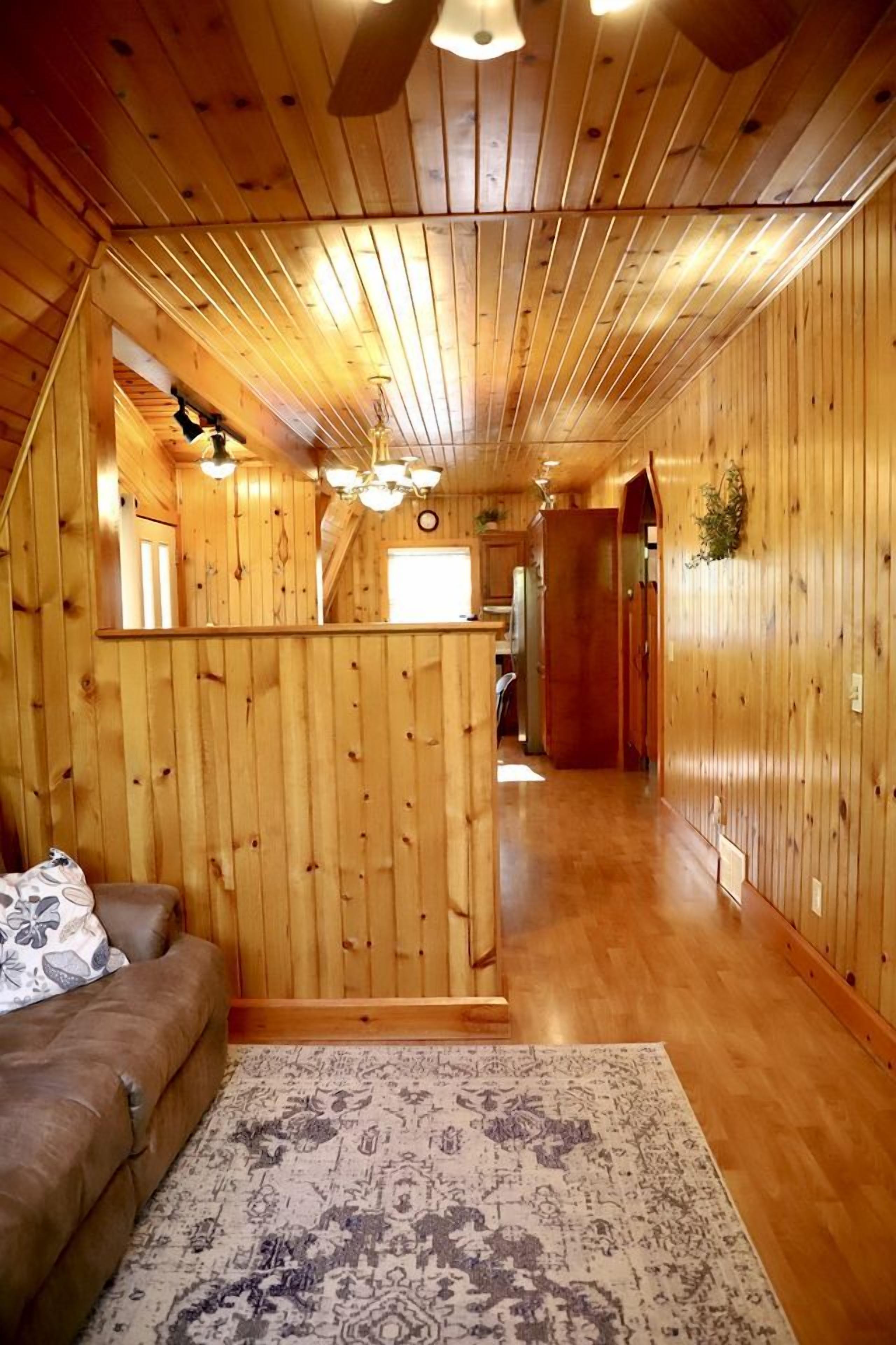 Een houten interieur met een bank, vloerkleed en een gang die leidt naar een keukenhoek.