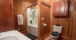 Et badeværelse med træpaneler, en glasafskærmet bruseniche, toilet og badekar.