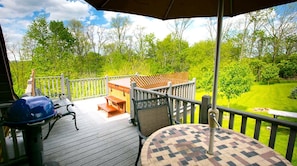 A covered deck with a table and chairs, a grill, and a view of a grassy yard.