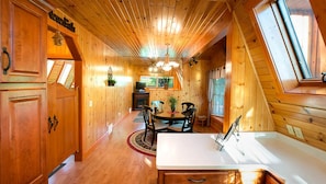 A wooden cabin interior with a dining area, a kitchen, and a loft bedroom.