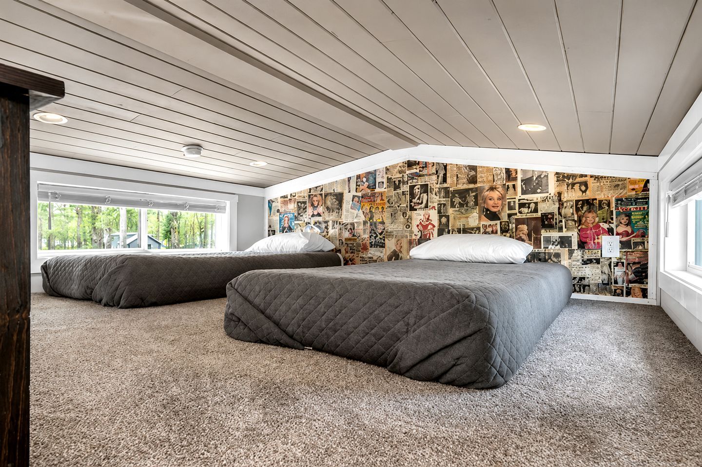 Una camera da letto con due letti, un soffitto spiovente e una parete ricoperta di fotografie.