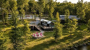En stuga vid sjön med en veranda, en eldstad och en liten sittplats utomhus.