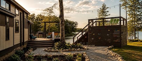 Une terrasse en bois avec des sièges extérieurs, un escalier menant à une autre terrasse, et une vue sur un lac.