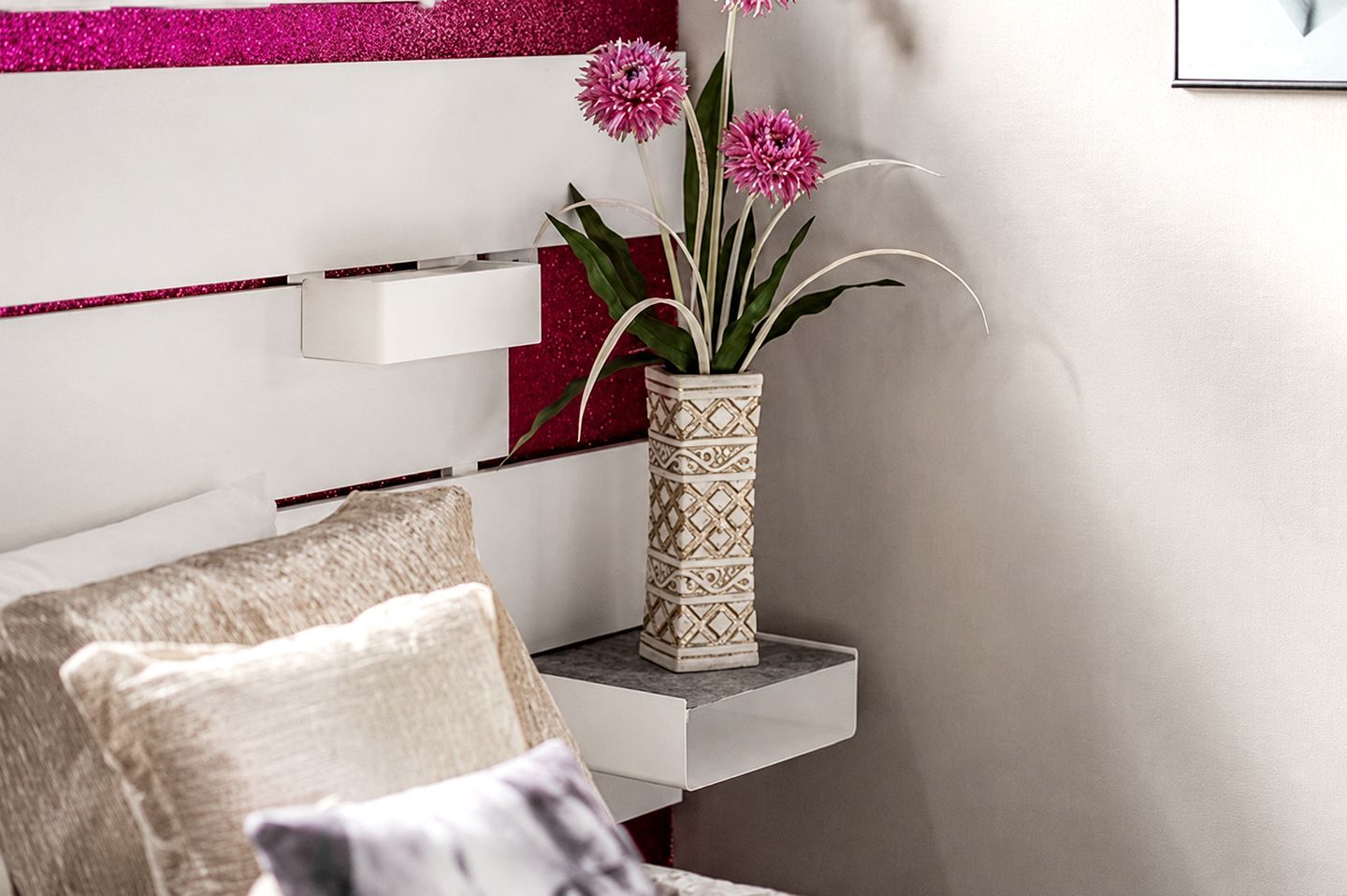 A white bedside table with a decorative vase containing pink flowers.