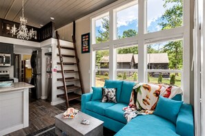 A modern kitchen with a built-in oven and microwave, a wooden ladder, and a blue sofa with a colorful throw blanket.