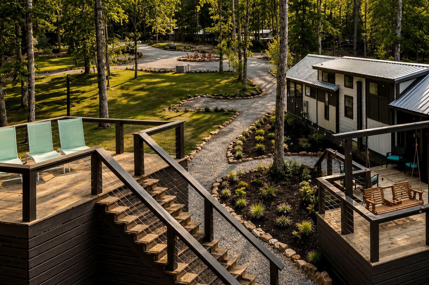 Una terraza de madera con mobiliario exterior, un sendero de grava y un edificio con techo de metal.