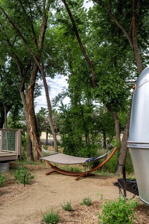 A hammock under a tree, a grill, and a portable toilet in a wooded area. - Prescott AZ Airstream Getaway One Block from Whiskey Row (Prescott)