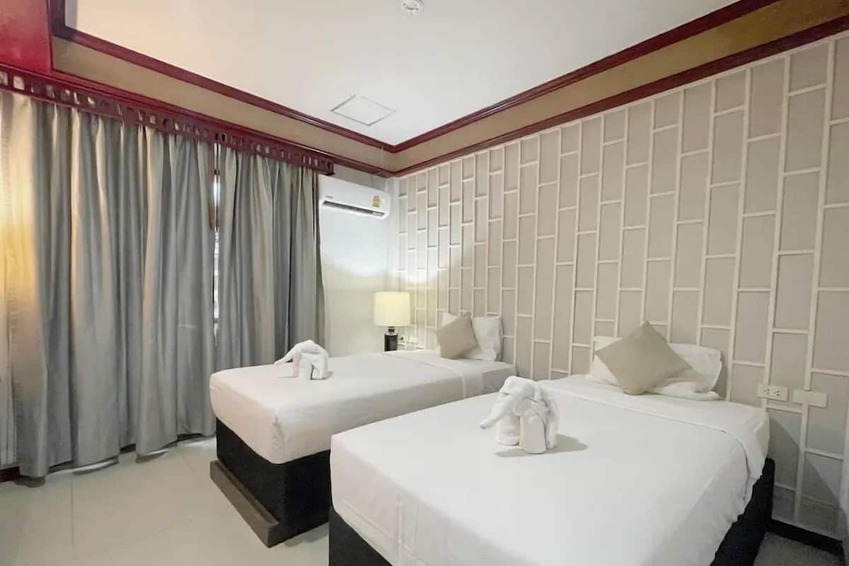Une chambre d’hôtel avec deux lits, un miroir, une fenêtre avec des rideaux et un mur orné d’un motif géométrique.