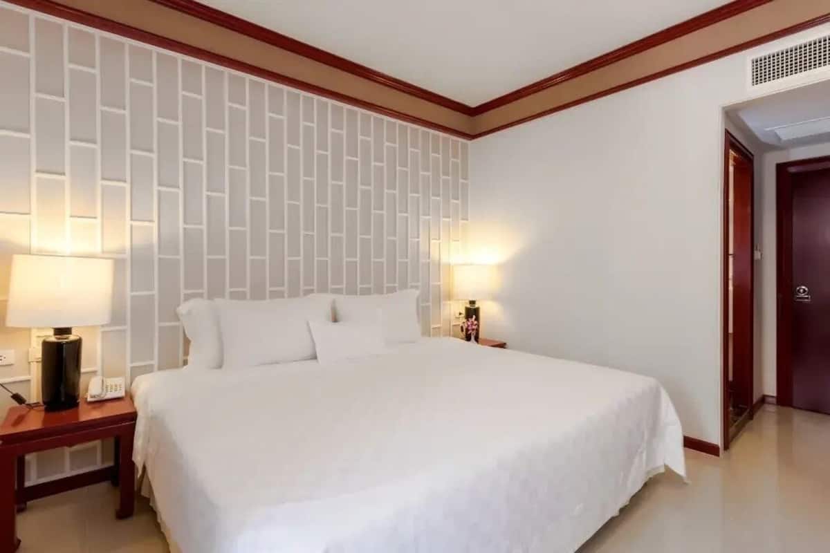 Une chambre d’hôtel avec un grand lit, deux tables de chevet avec des lampes, un mur orné d’un motif géométrique et une porte.