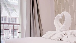 A hotel room with a bed, a view of a building with balconies, and a window with curtains. - Liberety Patong Resort (Patong)