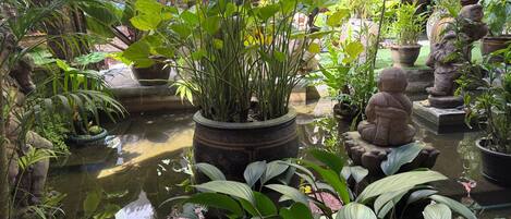 Un jardin intérieur paisible, avec un bassin, des plantes en pot et des statues de pierre.
