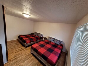 A room with two wooden beds, a ceiling light, and a window with blinds. - Gorgeous Cottage with Stunning Sights in Wellston, Michigan (Wellston)