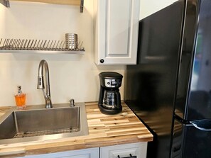 A kitchen with a stainless steel sink, a coffee maker, and a black refrigerator.