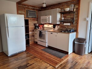 Eine kleine Küche mit Kühlschrank, Mikrowelle, Backofen und Holzschränken.