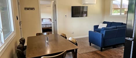 A dining area with a table and chairs, a blue sofa, a ceiling fan, and a TV mounted on the wall.